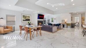 Een ruime woonkamer met een eettafel, banken, een open haard en een aan de muur bevestigde televisie.