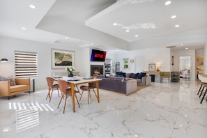 Un salón espacioso con una mesa de comedor, sofás, chimenea y televisor montado en la pared.