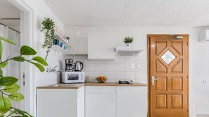 Una cocina compacta con armarios blancos, una puerta de madera y una pequeña encimera con un hervidor y un cuenco de fruta.