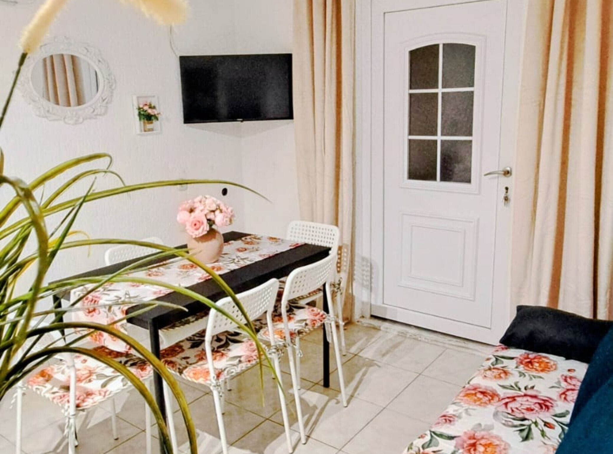 A room with a dining table, chairs, a TV mounted on the wall, a door, and a large potted plant.