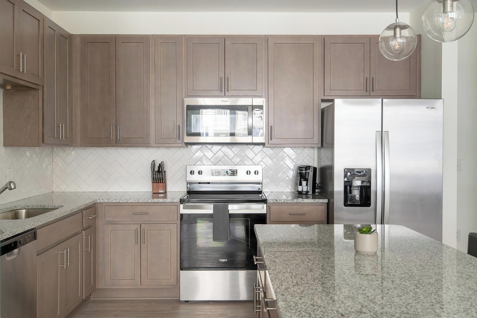 Una cocina moderna con electrodomésticos de acero inoxidable, un salpicadero de baldosas tipo espiga y armarios de madera.