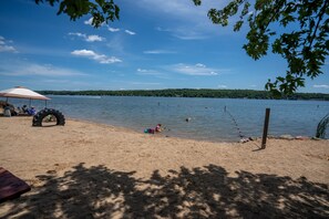 A beach with a tire barrier, a picnic table, and a person kayaking. - Steps to Lake Como! Intimate Getaway Lake Geneva! (Lake Geneva)