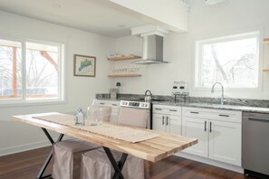 A modern kitchen with white cabinets, a wooden table, a gas stove, and a dishwasher. - Steps to Lake Como! Intimate Getaway Lake Geneva! (Lake Geneva)