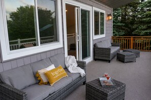 A covered outdoor seating area with a grey sofa, wicker chairs, and a small table with a drink. - Steps to Lake Como! Intimate Getaway Lake Geneva! (Lake Geneva)