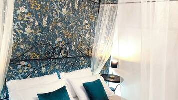 A bed with a floral headboard, a bedside table with a lamp, and sheer curtains.