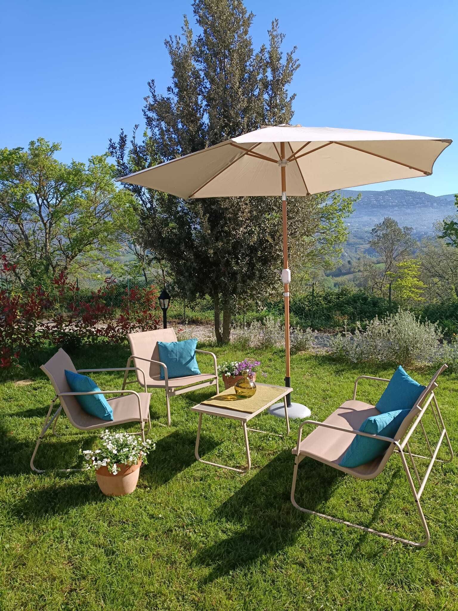 An outdoor seating area with a table and chairs, a large umbrella, and a view of a hilly landscape.