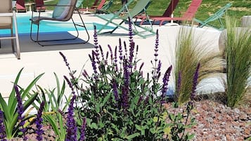 A pool area with lounge chairs and umbrellas, surrounded by plants and a view of hills.