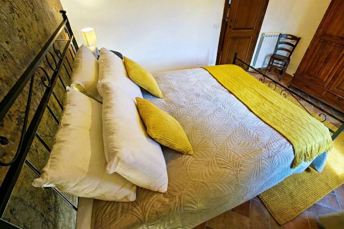 A bedroom with a bed, pillows, a bedside lamp, a wooden wardrobe, and a radiator.