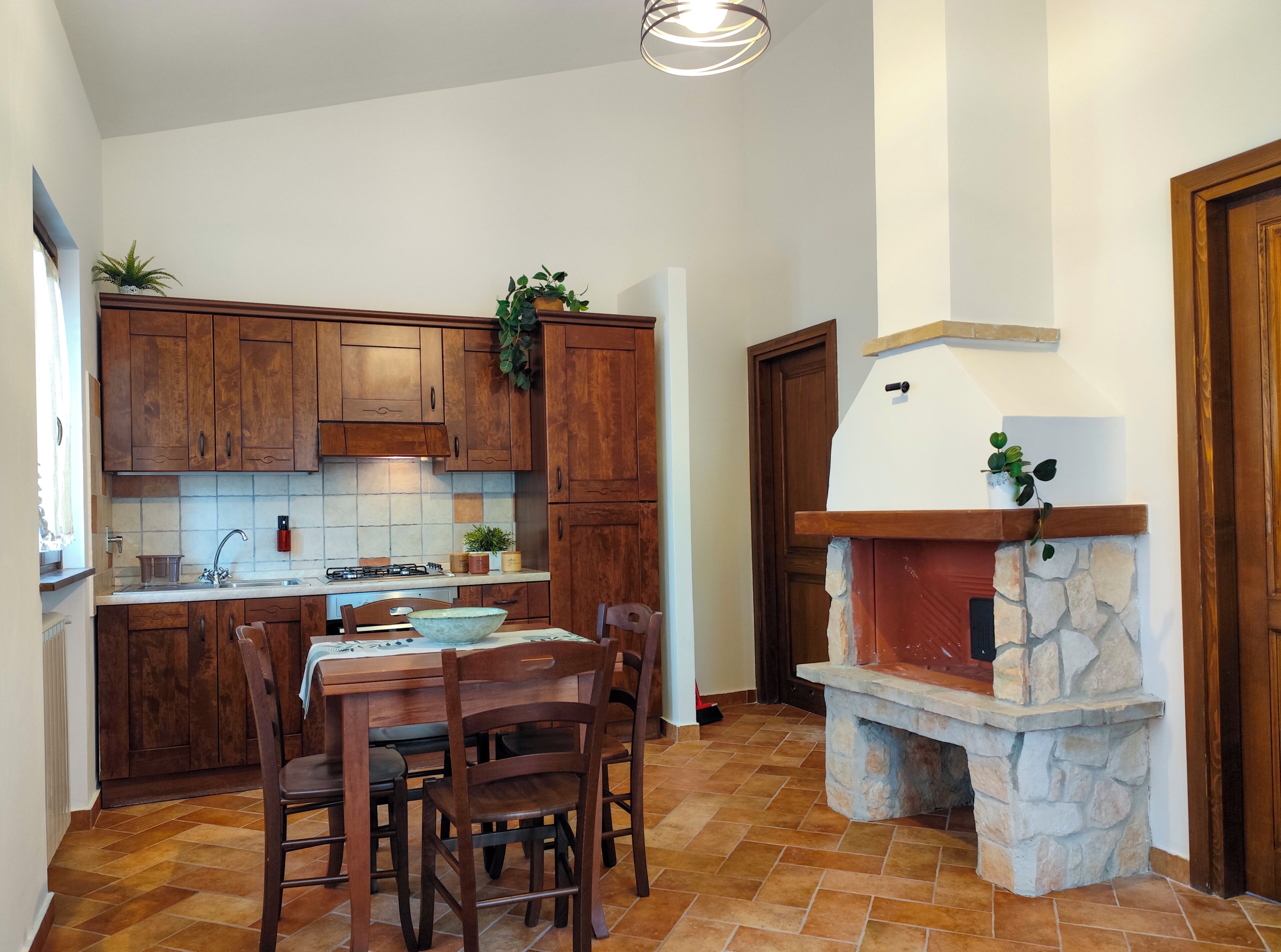 A kitchen with wooden cabinets, a stone fireplace, and a dining area with chairs.