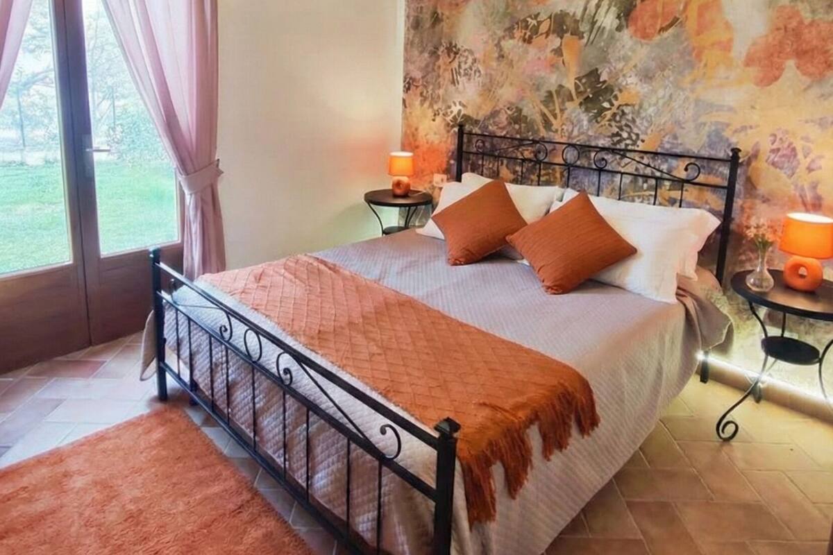 A bedroom with a bed, a window with curtains, a wall with a floral mural, and a floor with tiles.