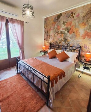 Ein Schlafzimmer mit einem Bett, einem Fenster mit Vorhängen, einer Wand mit floralem Wandbild und einem Fliesenboden.