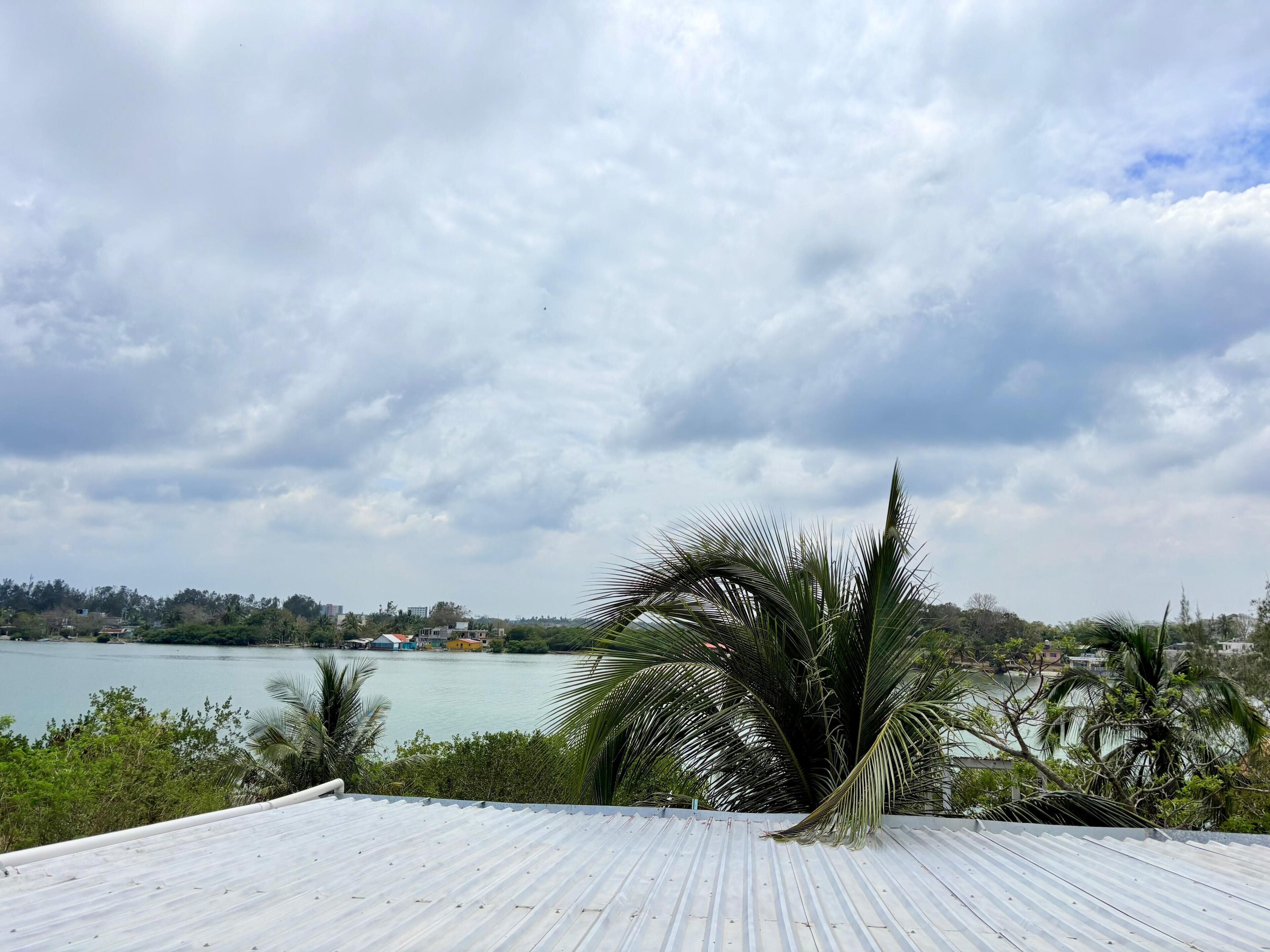 A view from a rooftop with a metal roof, overlooking a body of water and a distant shoreline with buildings.