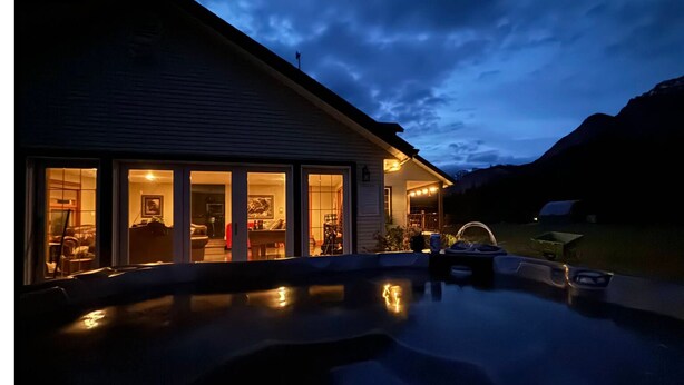 A house with a swimming pool at dusk, large windows, and a mountain backdrop.