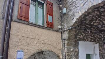 Un estrecho callejón con un arco de piedra, una puerta de madera y una ventana con contraventanas.