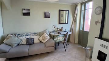 Una sala de estar con sofá, mesa de comedor, sillas, lámpara, reloj y chimenea.