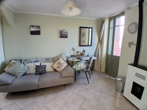 A living room with a sofa, a dining table, chairs, a lamp, a clock, and a fireplace. - Elegant Bajardo Apartment With Stunning Views (Bajardo)