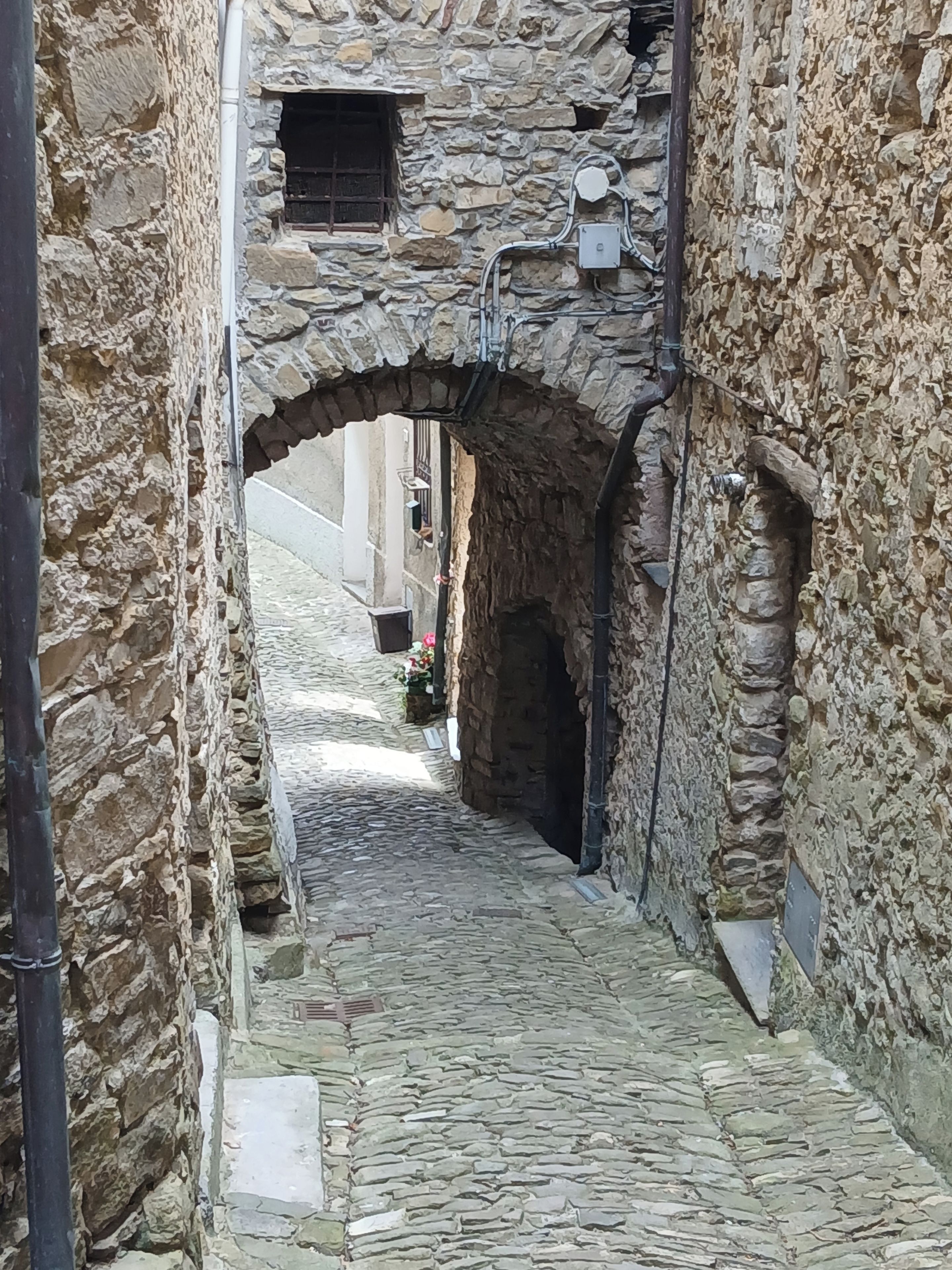 Ein schmaler Steinweg führt an einem rustikalen Steinhaus mit rundem Durchgang vorbei.