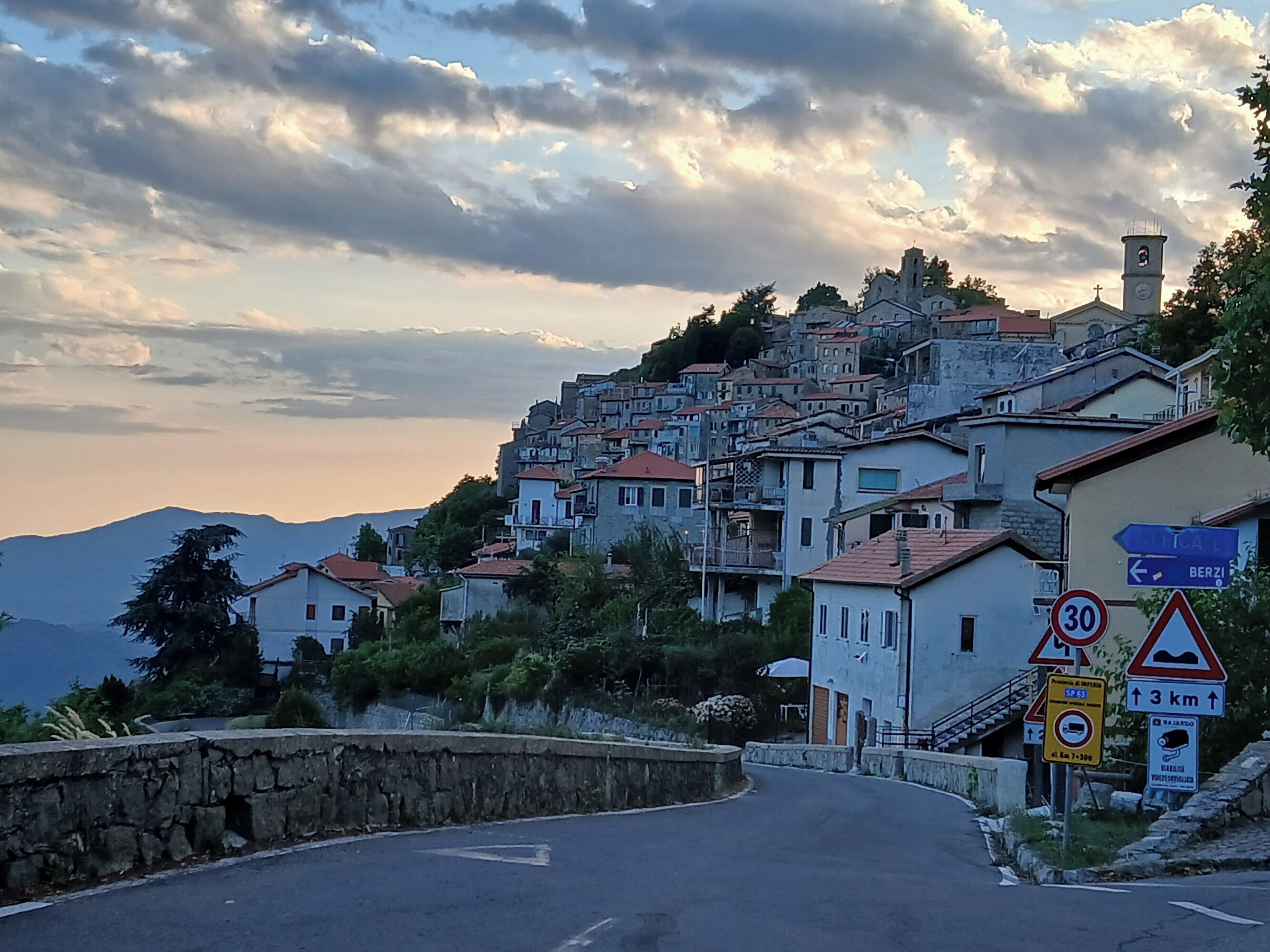 A hillside village with buildings, a winding road, and various road signs.