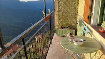 Un balcón con vistas a un paisaje montañoso, una mesa con un cuenco y una taza, y un panel de celosía verde.