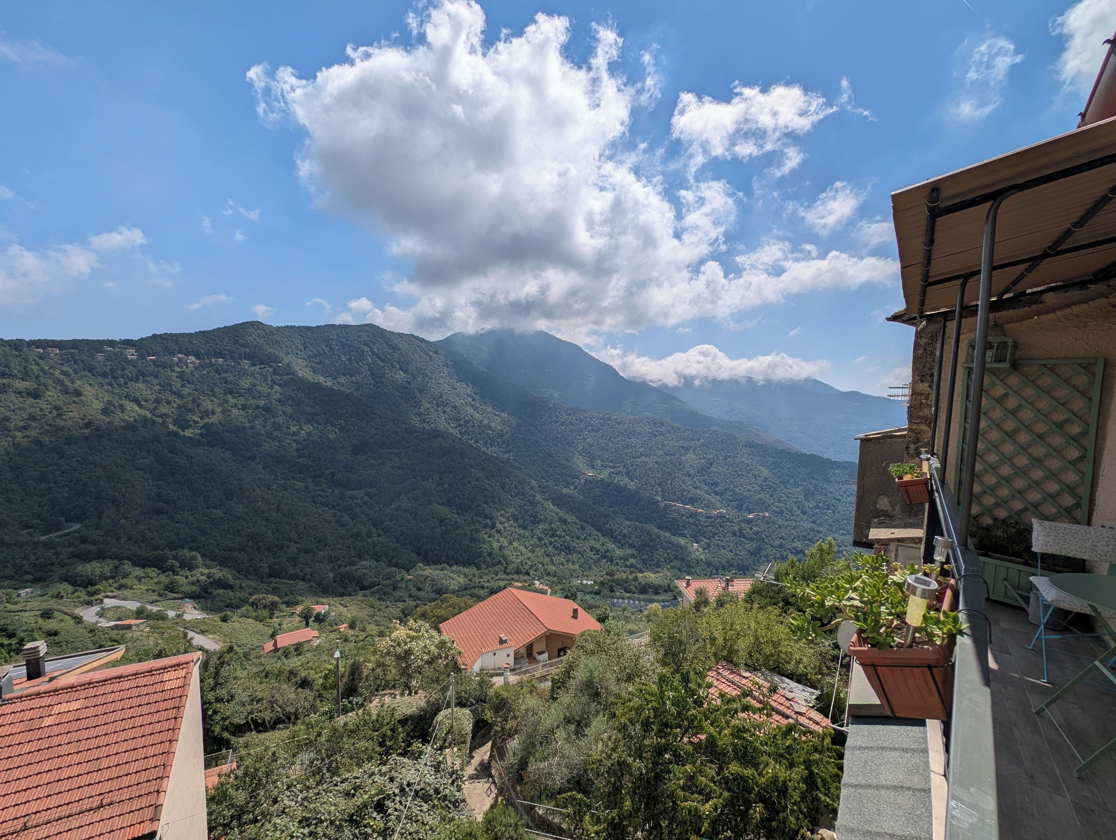Un paysage montagneux, avec un ciel dégagé, un bâtiment à toit rouge et un balcon orné de plantes en pot.