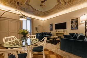 A living room with a glass table, white chairs, a blue sofa, a fireplace, and a TV mounted on the wall. - Spada Boutique Frescoed Luxury Suite with Elevator (Firenze)