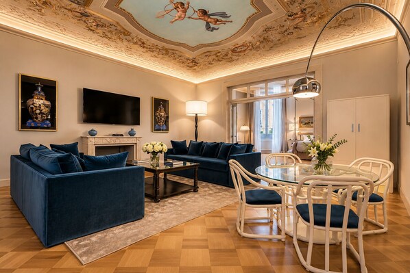 A living room with a sofa, coffee table, and dining area with chairs. - Spada Boutique Frescoed Luxury Suite with Elevator (Firenze)