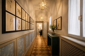 A hallway with framed botanical prints, a star-shaped light fixture, a green console table with a vase, and a checkered floor. - Spada Boutique Frescoed Luxury Suite with Elevator (Firenze)