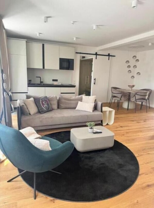 A modern living room with a sofa, a blue armchair, a coffee table, and a dining area with a table and chairs.