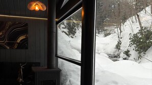 A room with a large window overlooking a snowy landscape, a fireplace, and a deer statue. - Ayder Dağ Evleri Elizan (Camlihemsin)