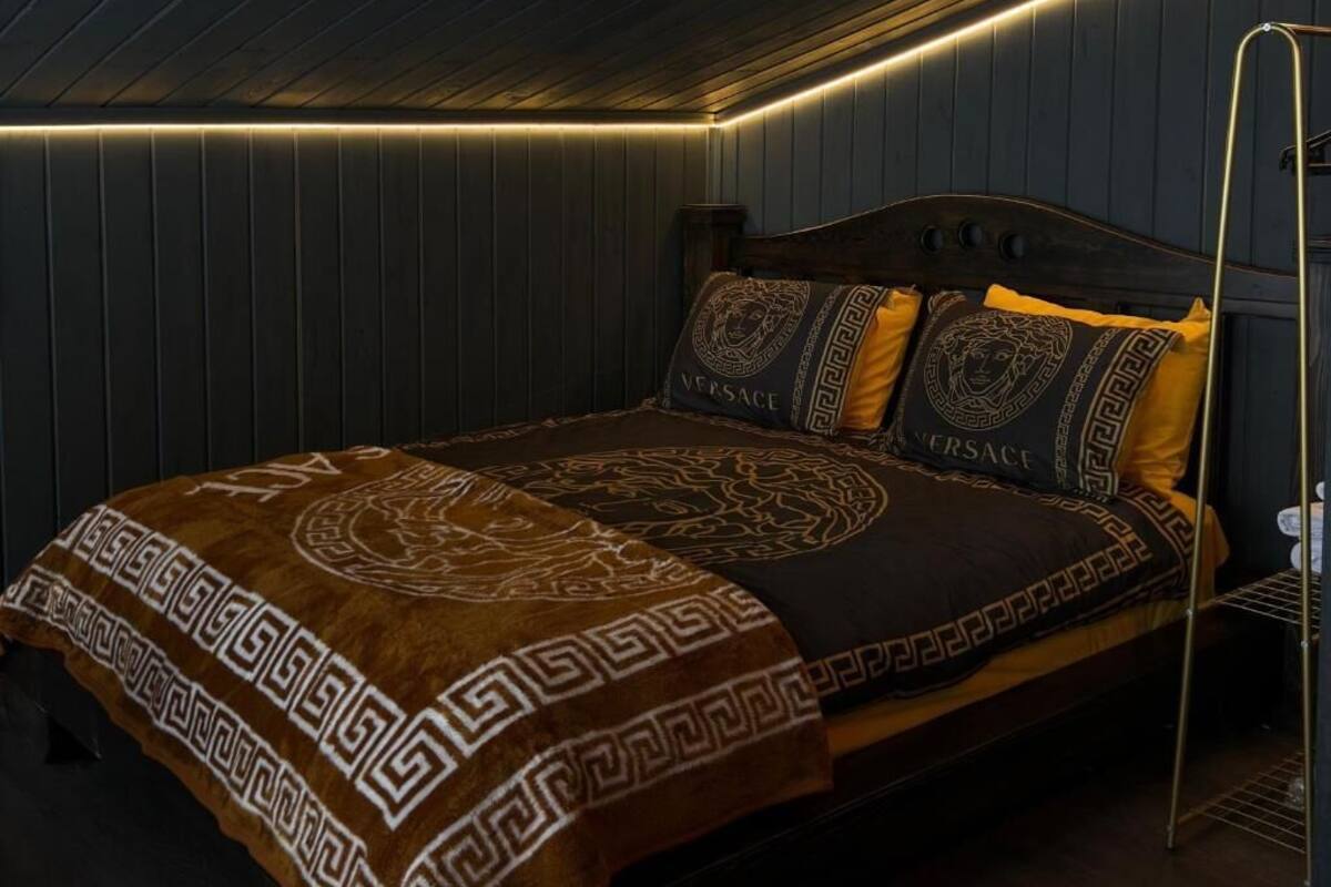 A bed with a patterned blanket, a headboard, and two pillows with a logo.