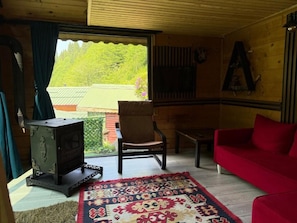 L’intérieur d’un chalet en bois, avec un canapé rouge, un tapis à motifs, une chaise, une petite table et un poêle à bois.