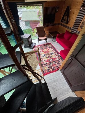 Un intérieur en bois avec un canapé rouge, un tapis à motifs, un fauteuil et une petite table sur laquelle se trouve un radiateur.