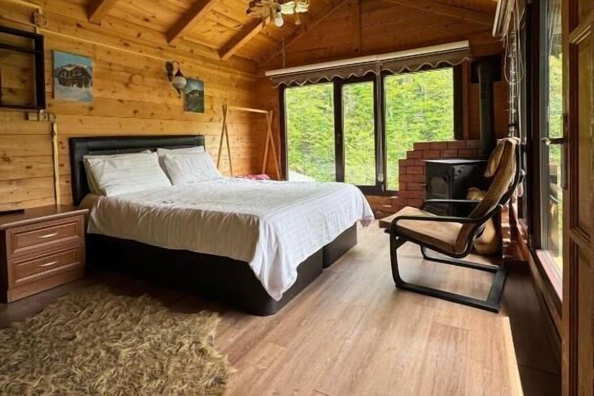 A wooden cabin bedroom with a bed, a chair, and a fireplace.