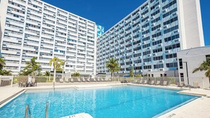 Una piscina con indicador de profundidad de 1.5 metros, rodeada de sillas de descanso y palmeras, con modernos rascacielos al fondo.