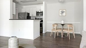 Eine moderne Küche mit weißen Schränken, Edelstahlgeräten und einem Essbereich mit rundem Tisch und Holzstühlen.