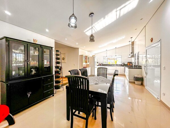 A modern kitchen with a dining area, featuring a black cabinet, a dining table with chairs, and pendant lighting. - Casa de Campo com Balan o na Rvore (Itapevi)