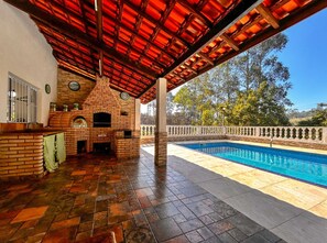 An outdoor patio with a brick fireplace, a pool, and a view of trees. - Casa de Campo com Balan o na Rvore (Itapevi)