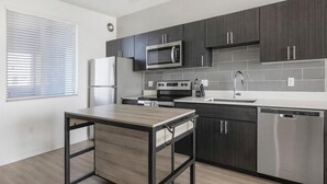 Een moderne keuken met donkere kastjes, een RVS magnetron, oven, vaatwasser en een klein houten tafeltje.