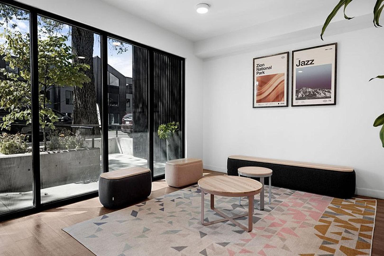 Een moderne kamer met grote ramen, een bank, twee ronde tafels en twee ingelijste foto’s aan de muur.
