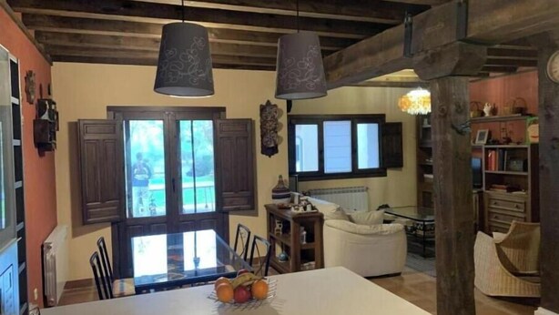 A spacious living area with a large central table, wooden beams, and a view of the outdoors. - El Acebo de Tanarro (Sepúlveda)