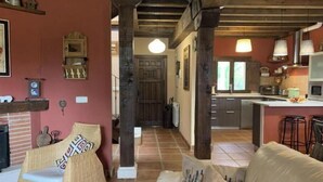 A cozy living room with a fireplace, wicker furniture, and a kitchen in the background. - El Acebo de Tanarro (Sepúlveda)