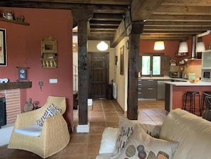Uma sala de estar aconchegante com lareira, móveis de vime e uma cozinha ao fundo.