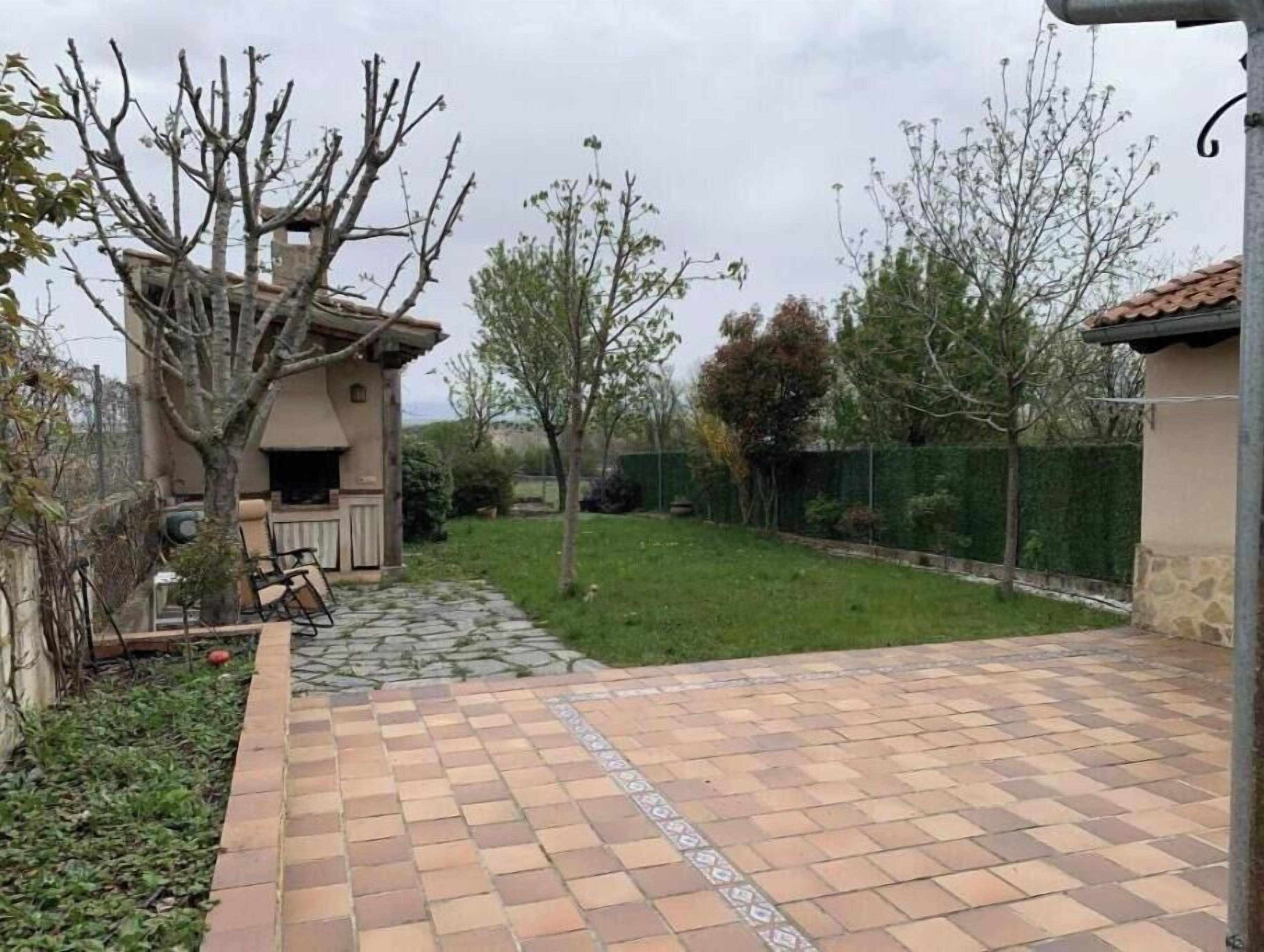 A patio with a patterned tile floor, a small outdoor seating area, and a view of a fenced yard with trees.