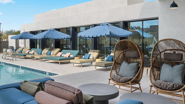 Un espace aménagé au bord de la piscine, avec des chaises longues et des parasols, une piscine, et un bâtiment moderne doté de grandes fenêtres.