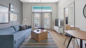 A modern living room with a sofa, coffee table, TV, and dining area. - Landing | Stylish 1BD, Rooftop Lounge, Gym (San Antonio)