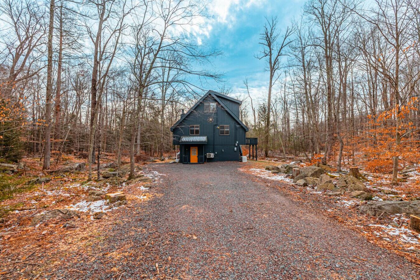 Une cabane avec une allée en gravier, entourée d’arbres et sous un ciel dégagé.