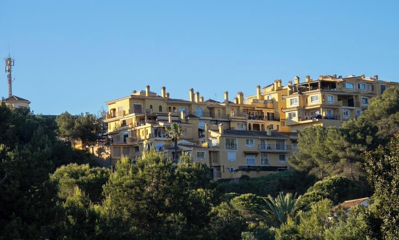 Edifício residencial com várias andares e varandas, cercado por vegetação.