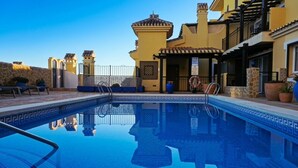 A swimming pool with a tiled edge, a stone wall, and a building with yellow and brown tones. - Luxury Duplex at La Manga Club Golf (Atamaría)
