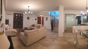 Uma sala de estar com sofá, mesa de centro e área de jantar com mesa de vidro e cadeiras.