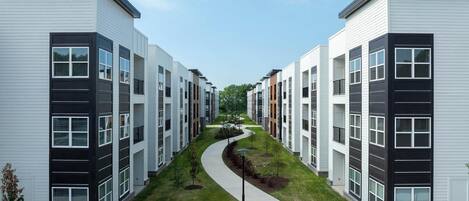 Un moderno complejo de apartamentos con un camino central, varios pisos y un diseño exterior uniforme.